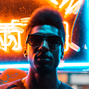 Headshot of man with sunglasses in front of neon sign
